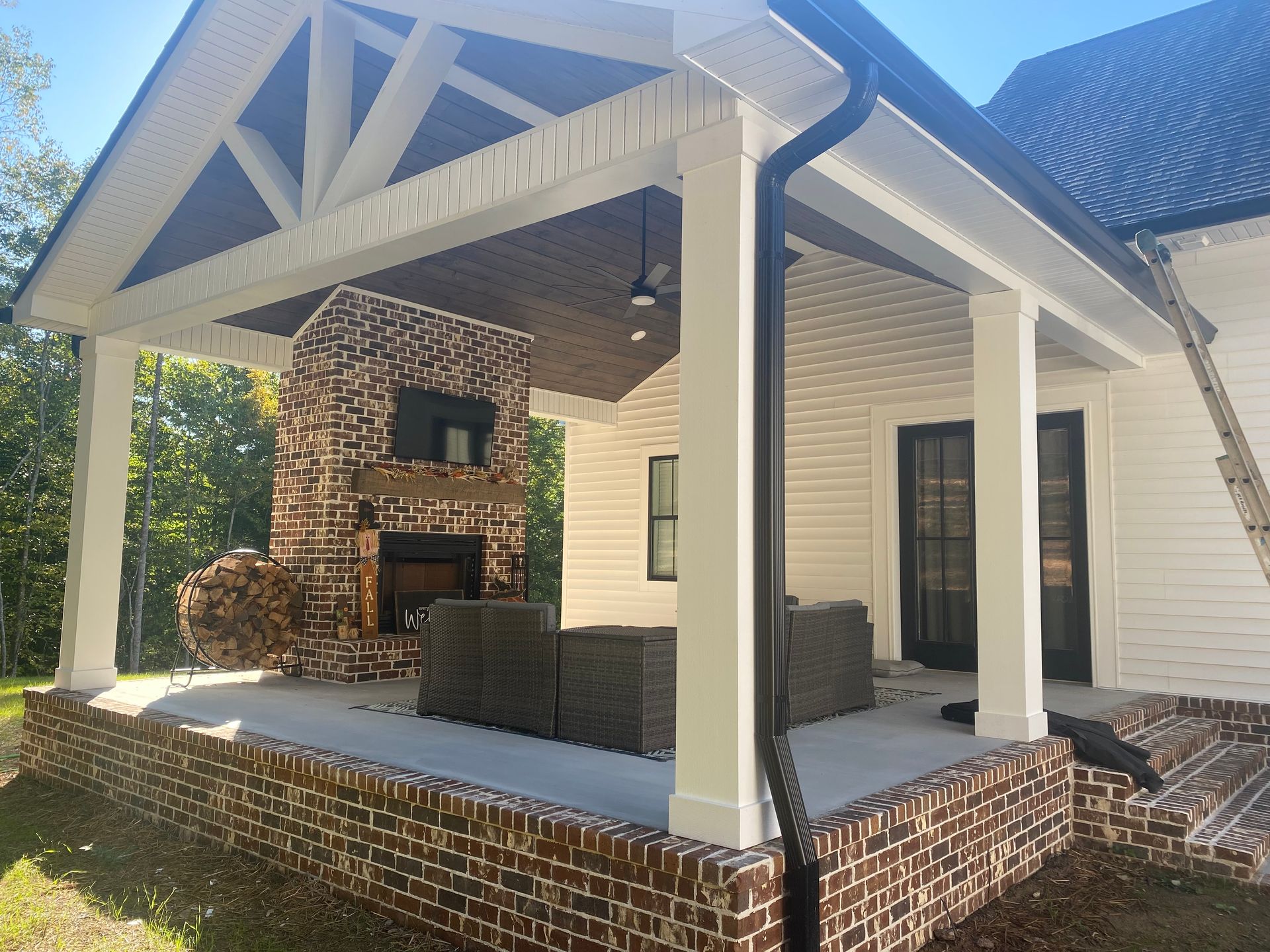 Covered brick patio with white columns, wicker seating, and a fireplace on a brick house porch