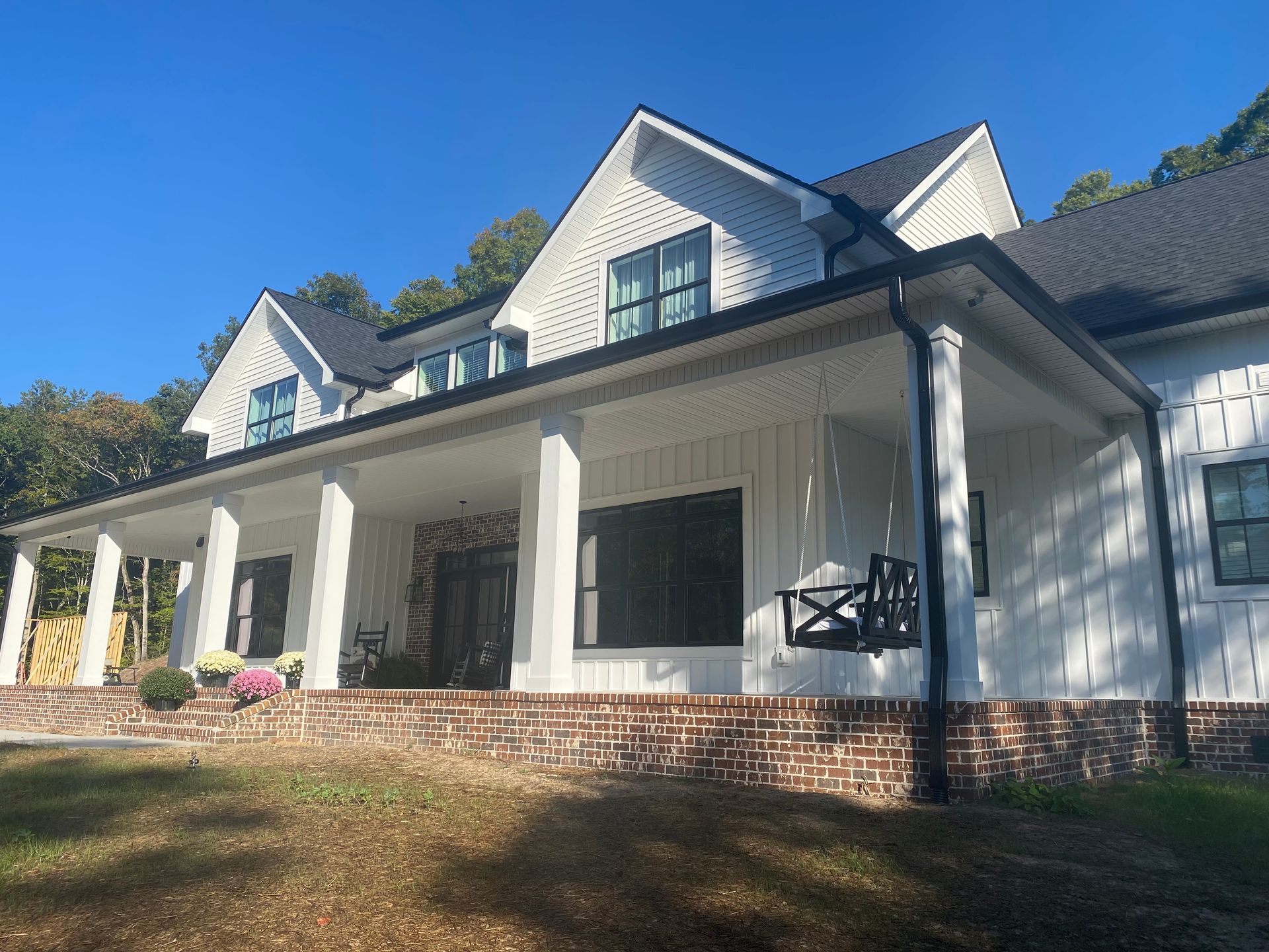 White house with a covered porch, dormer windows, and a brick foundation on a sunny day
