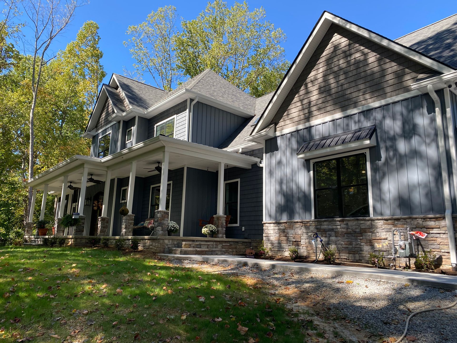 Gray house with a stone foundation and covered porch, surrounded by trees and lawn in daylight