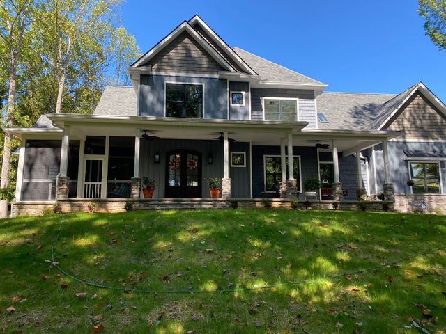 Gray house with front porch, white trim, and green lawn under a blue sky