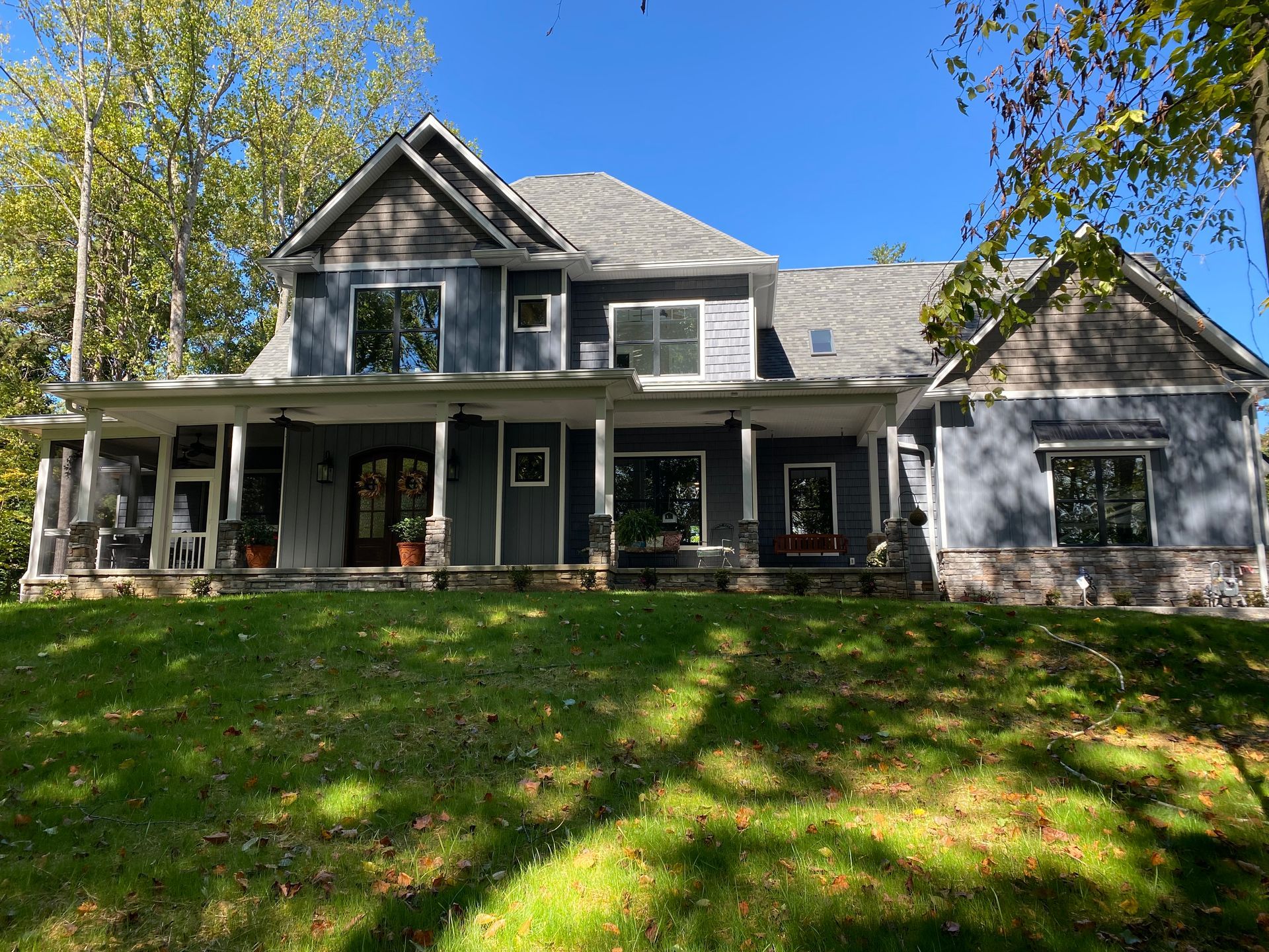 Gray two-story house with a front porch and detached garage, surrounded by trees and a grassy yard