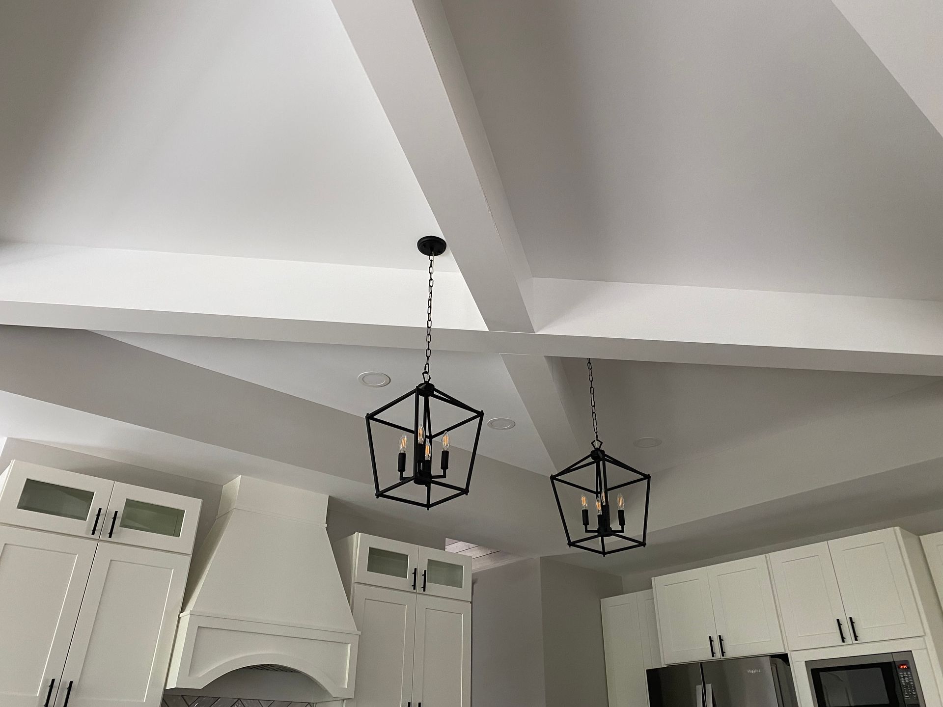 White vaulted kitchen ceiling with exposed beams and two black pendant lantern lights