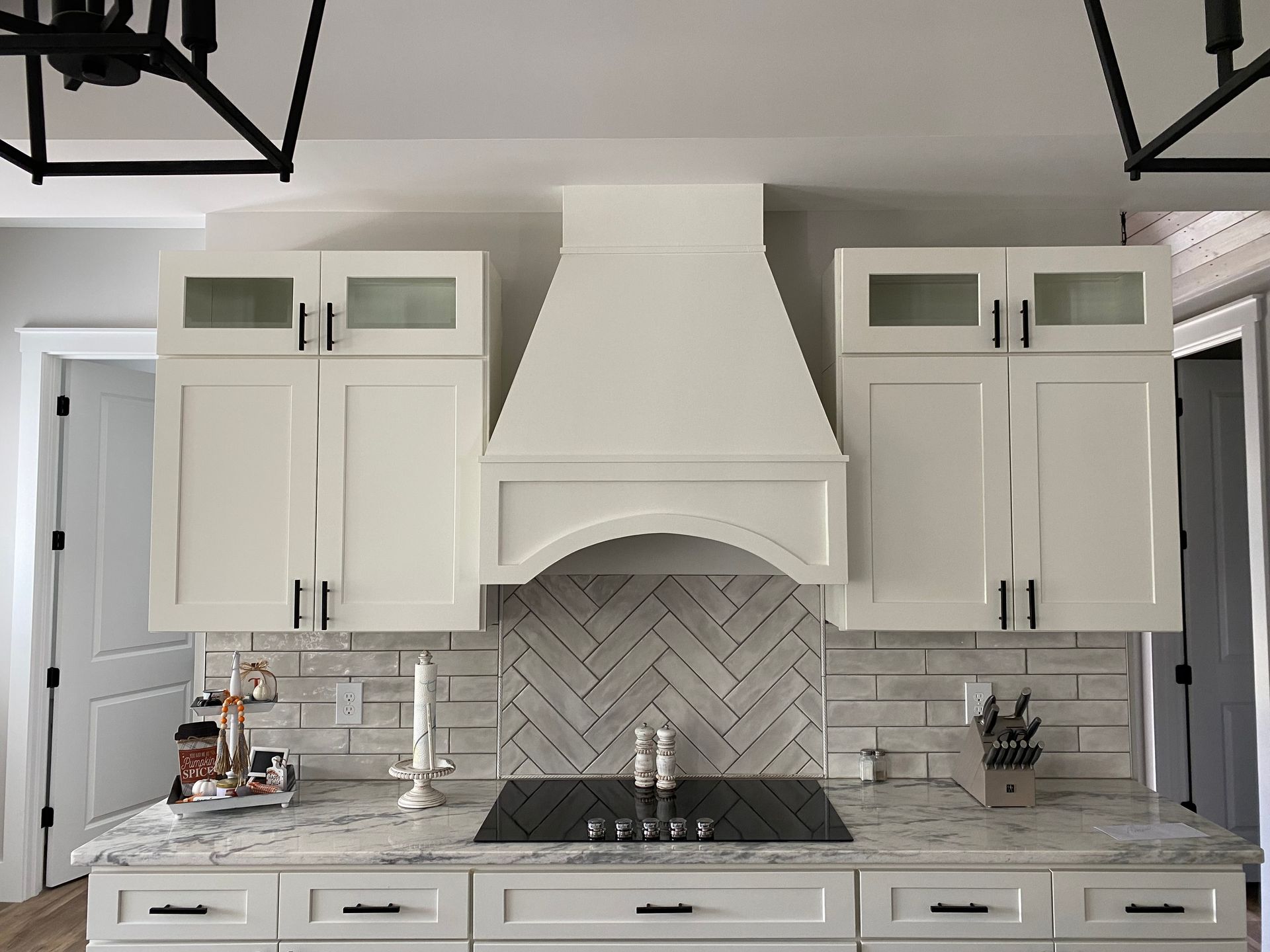 Bright white kitchen with large center range hood, herringbone backsplash, and long countertop cabinets.