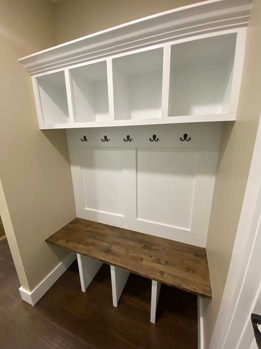 White mudroom bench with wood seat, hooks, cubbies, and overhead cabinets in a hallway