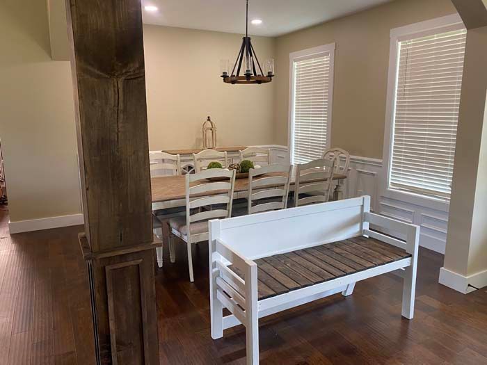 Dining room with white table and chairs, bench in foreground, hardwood floor, and pendant light by windows with blinds