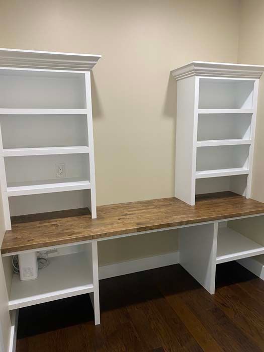 White shelving units on a wood countertop with open cabinets below in a room with hardwood floors