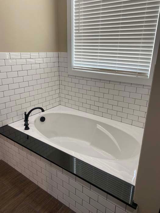Modern white subway-tile bathroom with a built-in white tub and black faucet under a window blind