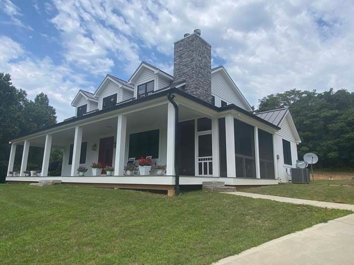 White farmhouse with wraparound porch on a grassy hill under a cloudy sky