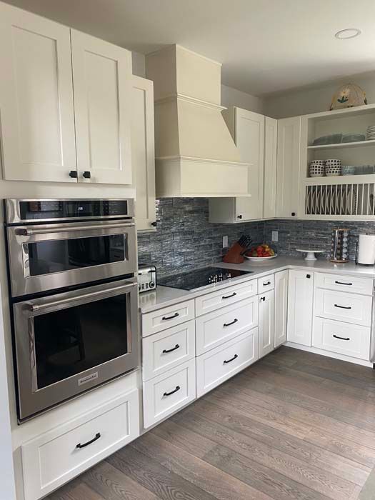 Bright white kitchen with built-in double oven, gray tile backsplash, and wood-look flooring