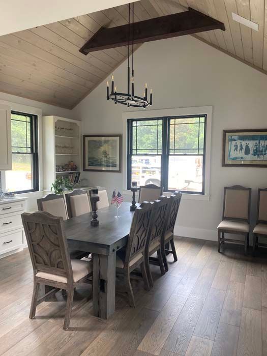 Dining room with wood table, upholstered chairs, and large windows under a vaulted ceiling