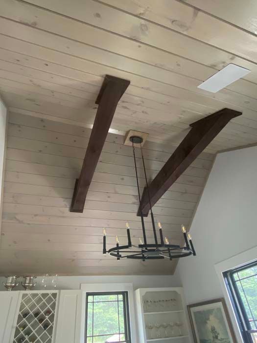 Ceiling with white planks, dark wooden beams, and a black chandelier over a bright room