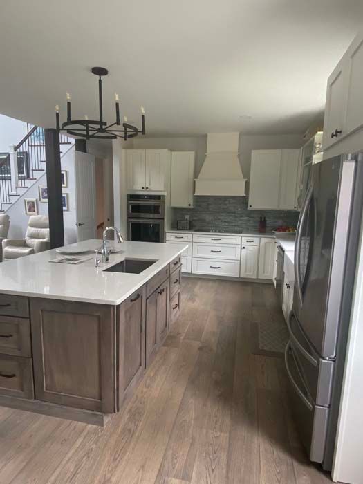 Modern kitchen with white cabinets, wood flooring, a large island, and stainless steel appliances.