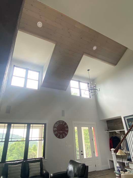 Bright living room with vaulted ceiling, large windows, ceiling fan, wall clock, and a black sofa