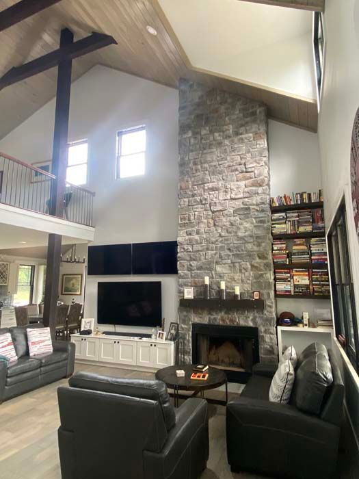 Spacious living room with tall stone fireplace, high ceiling, leather chairs, and wall-mounted TV