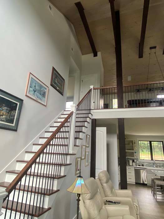 Living room with a staircase, high wood-beamed ceiling, and open view into the kitchen.