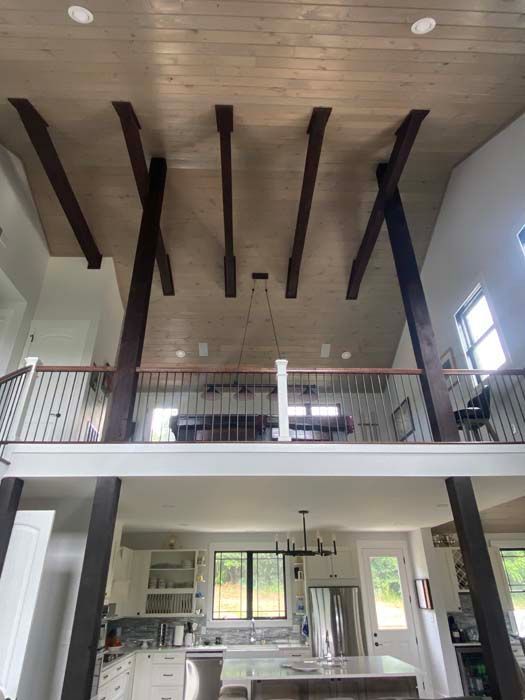 Modern loft interior with exposed wooden ceiling beams, open mezzanine, and bright kitchen below