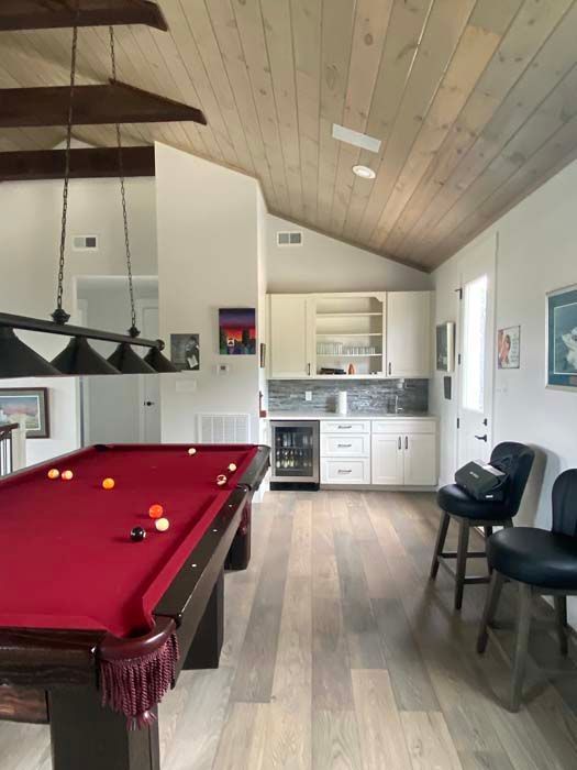 Game room with a red pool table, kitchen nook, and black chairs under a sloped wood ceiling
