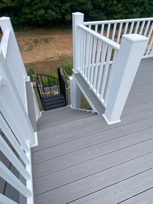 White outdoor stairway with gray steps leading down to a black metal gate and greenery below