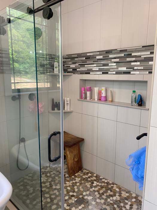 Modern tiled shower with glass door, mosaic floor, built-in shelf, and hanging blue towel