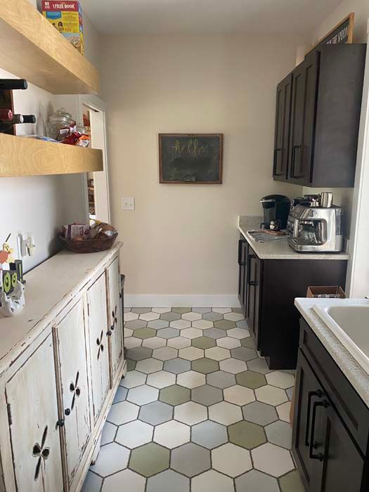 Narrow kitchen with white hex tile floor, dark cabinets, open shelves, and countertop appliances.