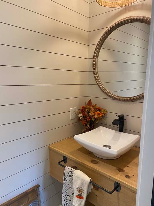 Small bathroom vanity with white sink, round mirror, wood counter, and a flower arrangement.