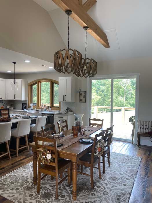 Dining room with rustic chandelier, wooden table, patterned rug, and sliding glass doors to a bright patio.