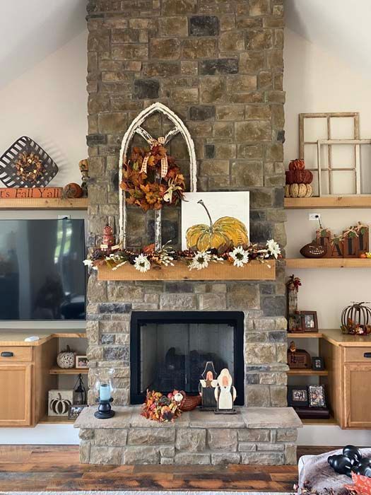 Stone fireplace decorated with autumn garland, pumpkins, and candles in a cozy living room