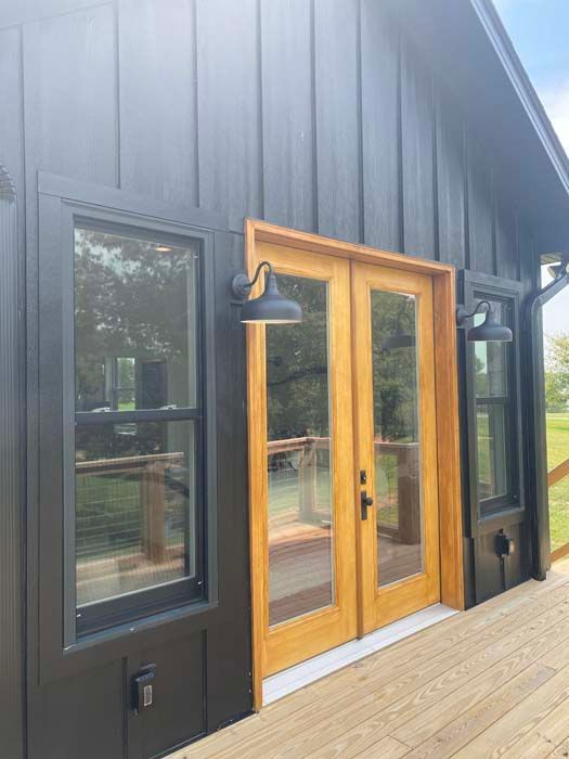 Black exterior of a modern building with a wooden-framed glass door and deck steps.