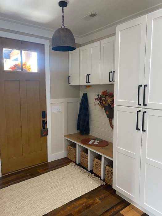 Entryway with wood front door, white built-in cabinets, bench, coat hooks, and a woven rug.