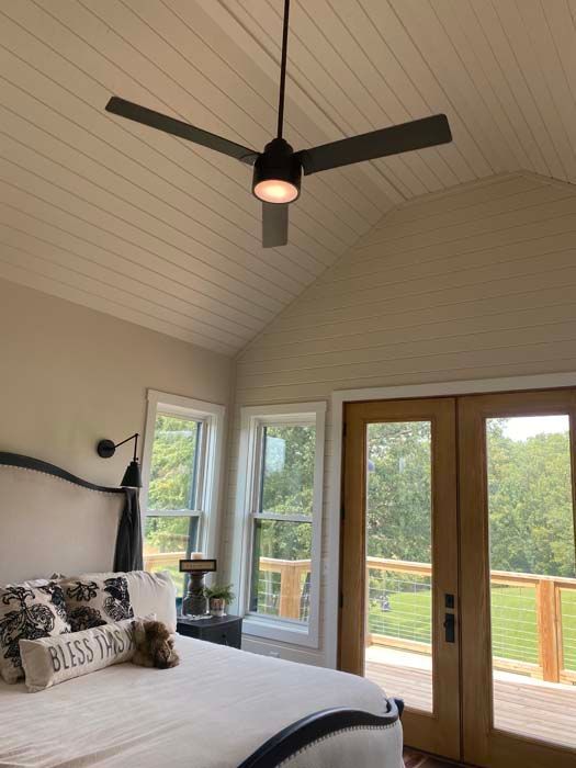Bedroom with vaulted ceiling, black ceiling fan, and French doors opening to a green view.