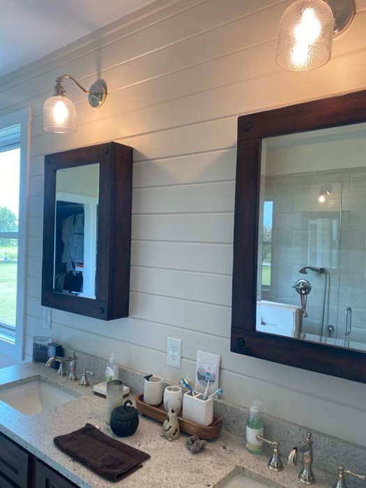 Modern bathroom vanity with two mirrors, wall sconces, and sink accessories on a white shiplap wall.