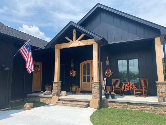 Modern house front porch with blue siding, wooden entry frame, stone steps, and an American flag.