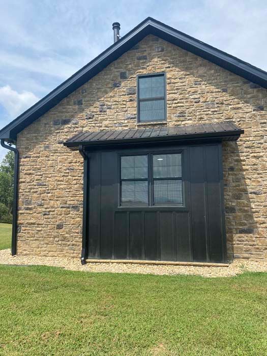 Stone house exterior with dark wood dormer and green lawn under a blue sky