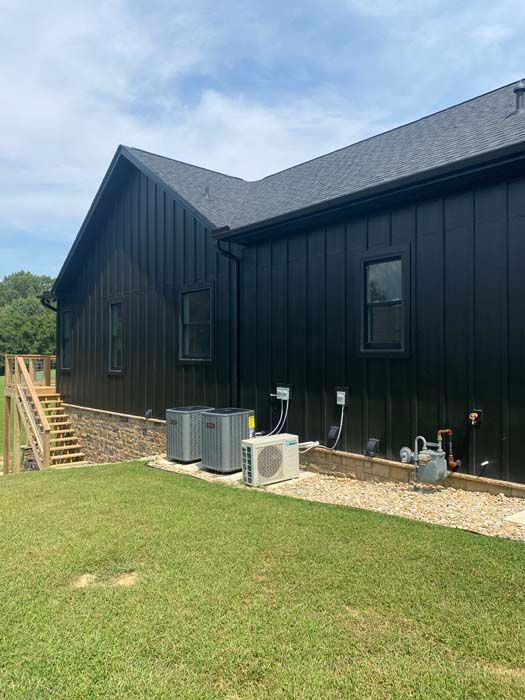 Black house exterior with HVAC units, side stairs, and grassy yard under a blue sky