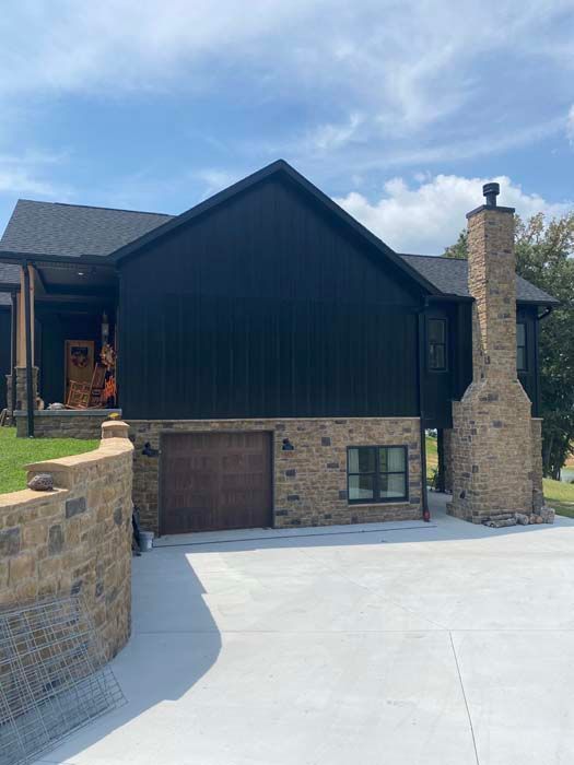 Modern house exterior with dark siding, stone chimney, and driveway under a blue sky