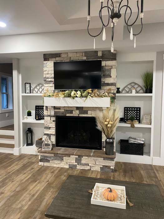 Modern living room with stone fireplace, mounted TV, built-in shelves, and wood flooring