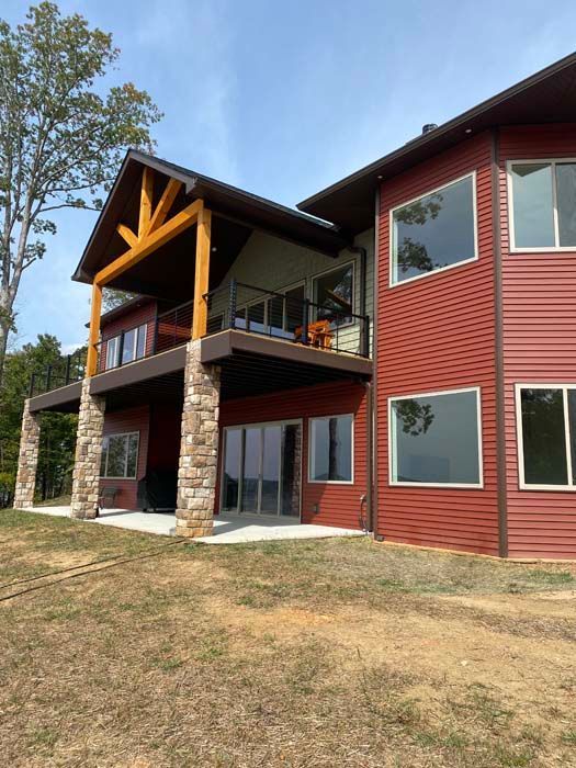 Two-story red house with stone columns, wood balcony, and a grassy yard
