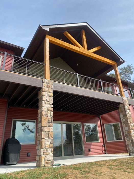 Rustic lodge exterior with stone pillars, red siding, and a covered balcony under a wooden gabled roof