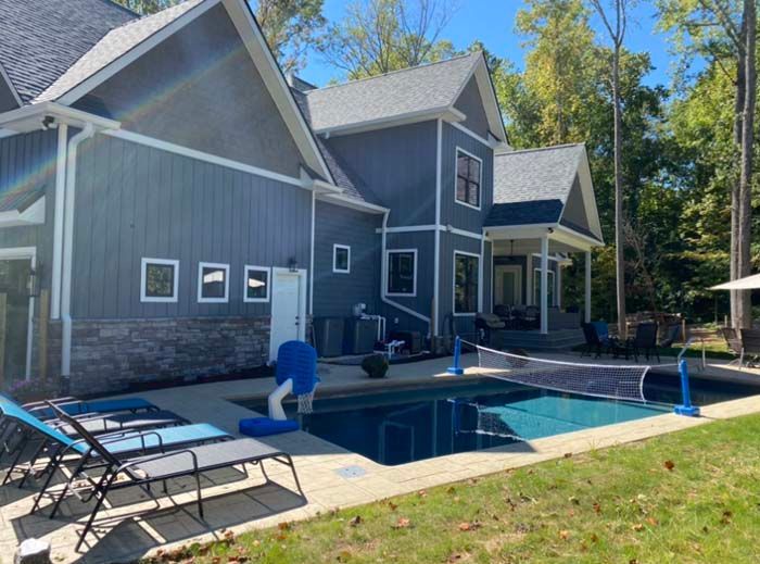 Backyard pool beside a gray two-story house with a patio and lounge chairs