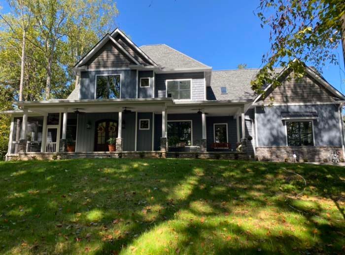 Large gray two-story house with wraparound porch and green lawn under a clear blue sky