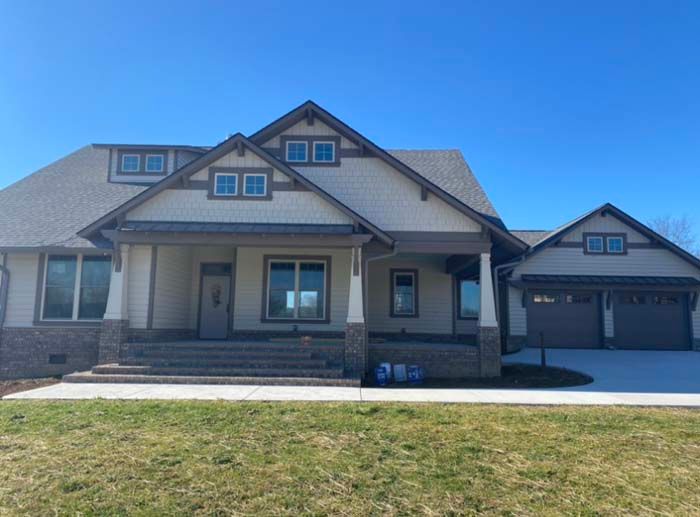 Modern two-story suburban house with gray siding, stone accents, front porch, and attached garage