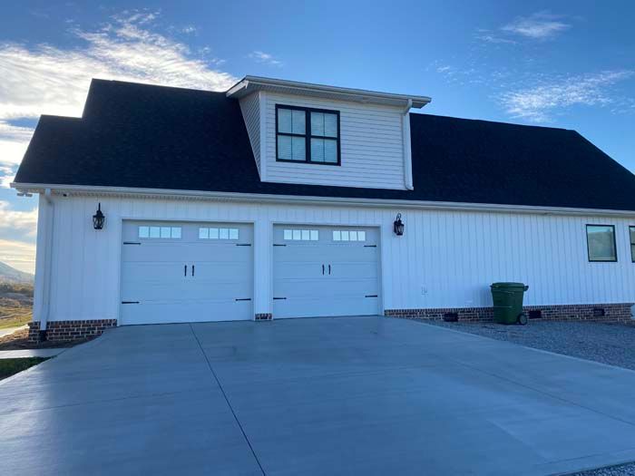 White two-story house with dark roof, double garage, and wide concrete driveway at sunset