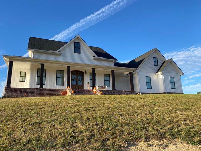 Single-story white house with black roof and front porch on a grassy hill under a blue sky