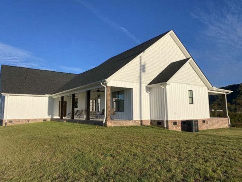 Single-story white house with a dark roof on a grassy hill under a clear blue sky
