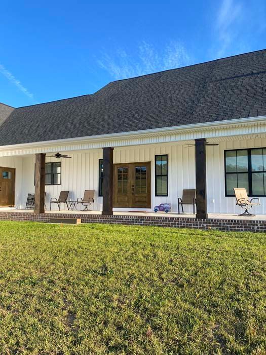 Single-story house with a dark roof, white porch, black columns, and lawn under a blue sky
