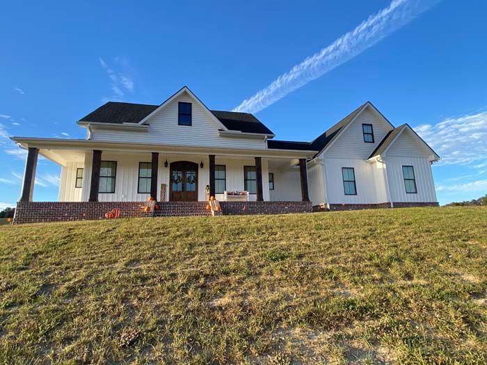 White farmhouse with a front porch on a grassy hill under a bright blue sky