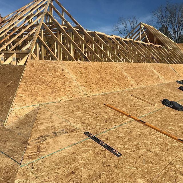 Roof trusses and plywood sheathing under construction on a house frame under blue sky