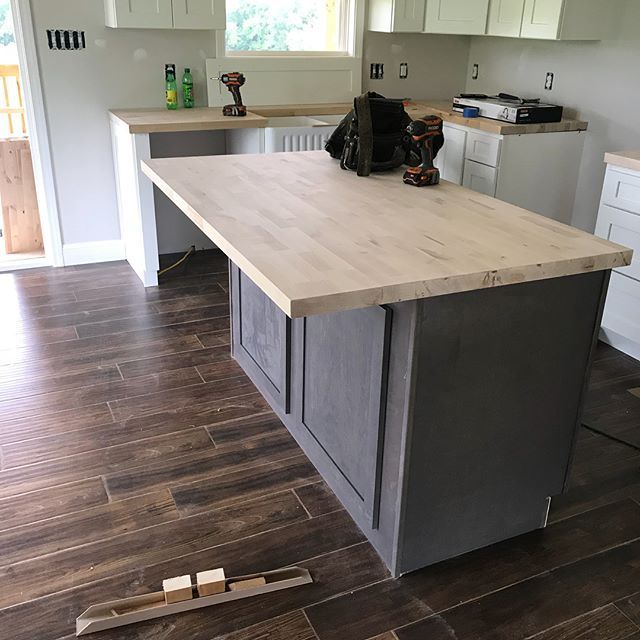 Kitchen with large gray island and light wood countertop on dark wood flooring, partially renovated.