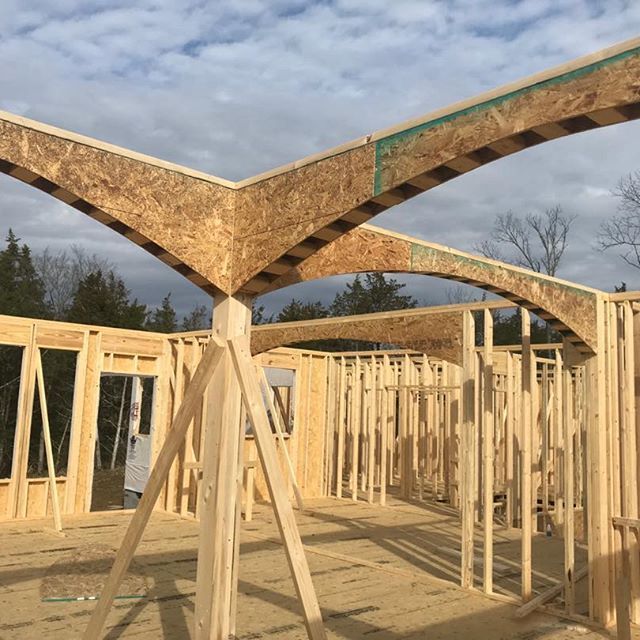 Wood-framed house under construction with exposed trusses against a cloudy sky