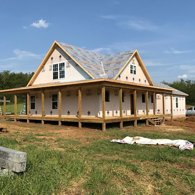 Partially built house with white siding and tan trim on a grassy lot under a blue sky